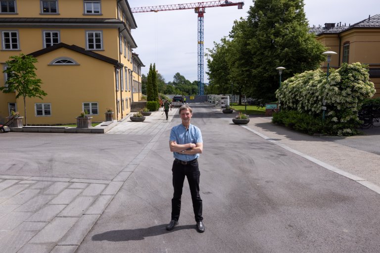 Styreleder Paul Erik Wirgenes står ute med armene i kors. I enden av veien bak ham, står en heisekran.